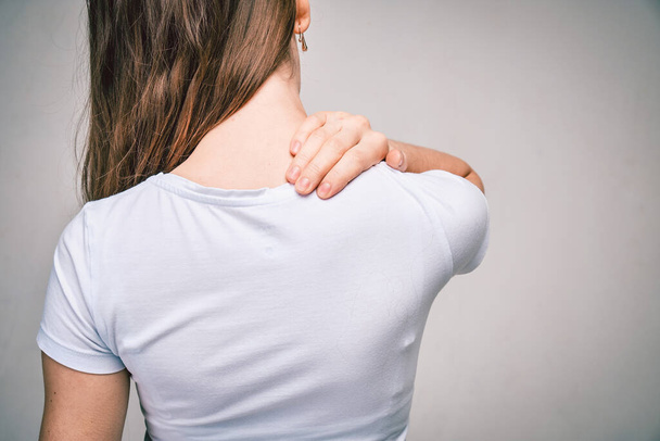 Een meisje in een wit T-shirt masseert haar nek van vermoeidheid. Sluiten.. - Foto, afbeelding