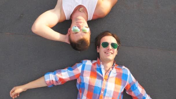 Vista superior de dos guapos gays en gafas de sol tumbados con alegría y expresión de alegría en la cara.Jóvenes hombres felices sonriendo y disfrutando de la vida juntos. Amigos relajándose al aire libre. Cámara lenta Primer plano
 - Metraje, vídeo