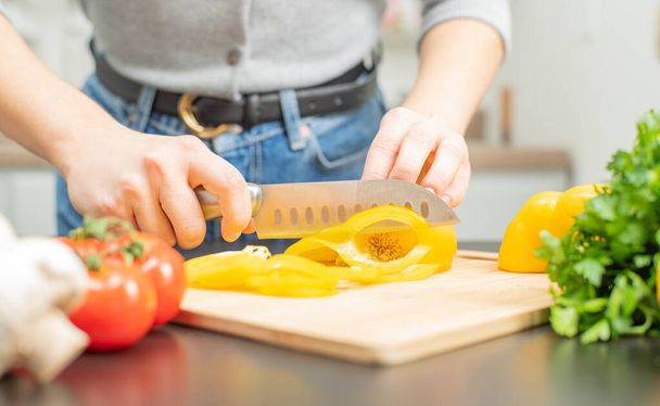 Woman is cutting yellow pepper on cut board on kitchen. Fresh vegetables for salad - Fotoğraf, Görsel