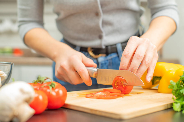 Woman is cutting tomatoes on cut board on kitchen. Fresh vegetables for salad - Фото, зображення