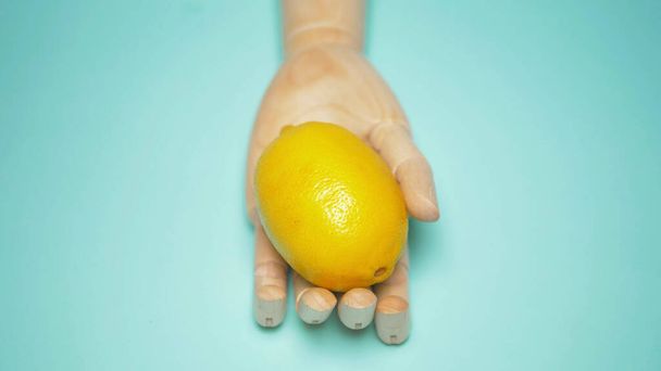 artificial wooden hand holding ripe yellow lemon. blue background - Fotoğraf, Görsel