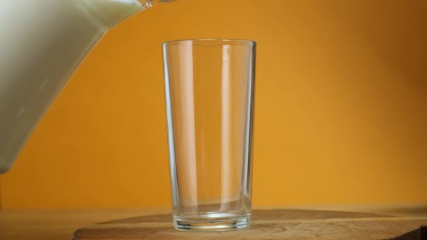 Close up Milch in Glas aus Glas auf Holzplatte mit farbigem Hintergrund gegossen. Nahaufnahme. - Filmmaterial, Video
