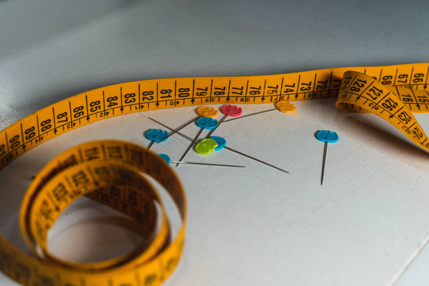 Žlutá měřicí páska a barevné jehly na bílém dřevěném stole - Fotografie, Obrázek