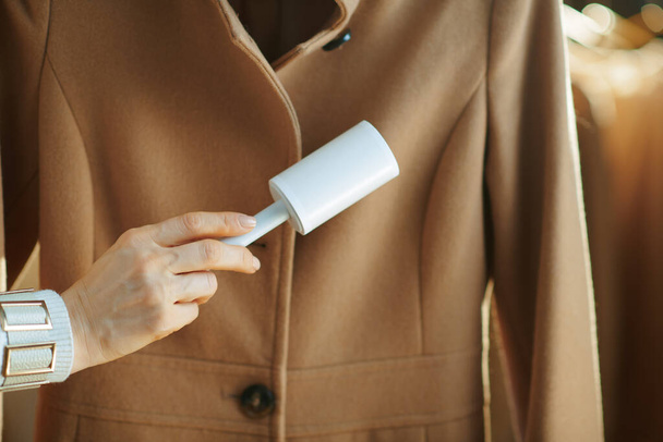 Preparing for cold season. Closeup on woman cleaning coat with lint roller in the living room in sunny winter day. - Photo, image