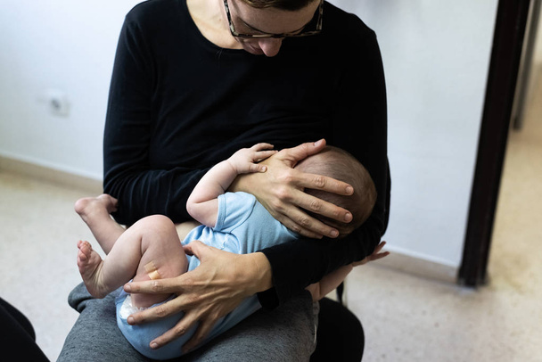 Bebé llorando después de la vacunación con tirita o yeso en el muslo, consolado por su madre que lo amamanta
. - Foto, Imagen