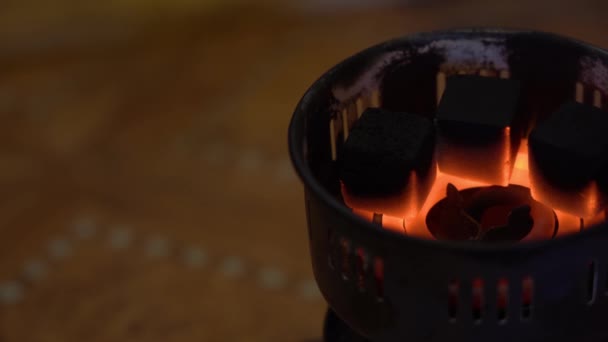 Carbón quemado y fundido en una vieja estufa eléctrica portátil especial de la red. 3 carbones cuadrados negros cocinan y se ruborizan en una espiral al rojo-caliente sobre un fondo marrón borroso cerca de la derecha
. - Imágenes, Vídeo