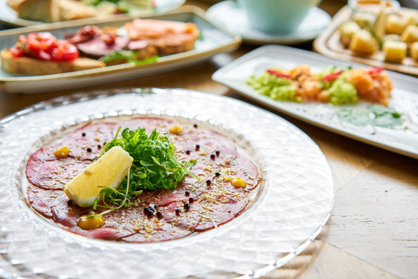 Beef carpaccio with balsamic caviar and Parmesan cheese. Various snacks and antipasti on the table. Italian cuisine Restaurant menu, natural and organic food concept. - Photo, Image
