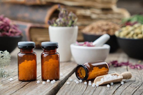 Bottles of homeopathic globules, books, mortars and bowls of healing herbs on background. Homeopathy medicine. - Valokuva, kuva