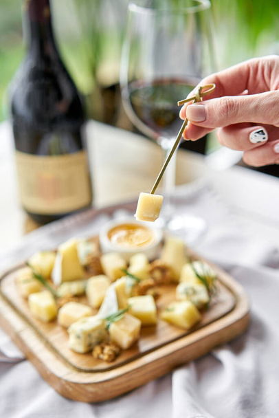 Meisje met stukje parmezaanse kaas op een spies en houten bord met kaas. Heerlijke kaasmix met walnoten, schat. Levensmiddelen voor wijn. - Foto, afbeelding