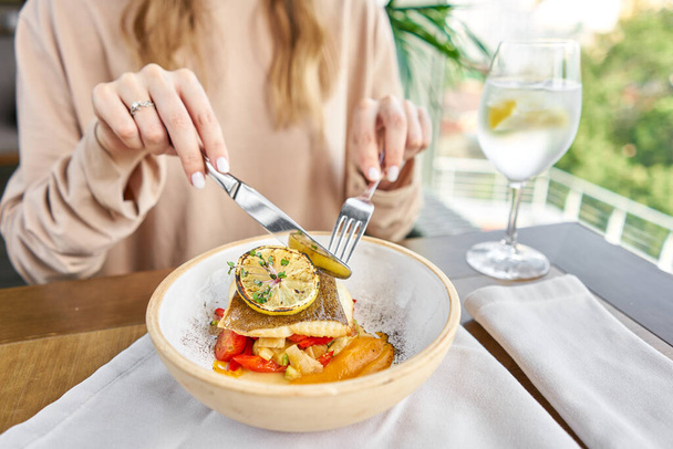 Жареный палтус с овощами, перцем и тыквенными сливками. Обед в ресторане, женщина ест вкусную и здоровую пищу. Блюдо украшено ломтиком лимона. Меню ресторана
 - Фото, изображение
