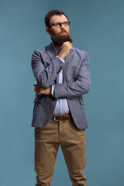 Pensive bearded man standing and thinking isolated on blue background - Foto, afbeelding