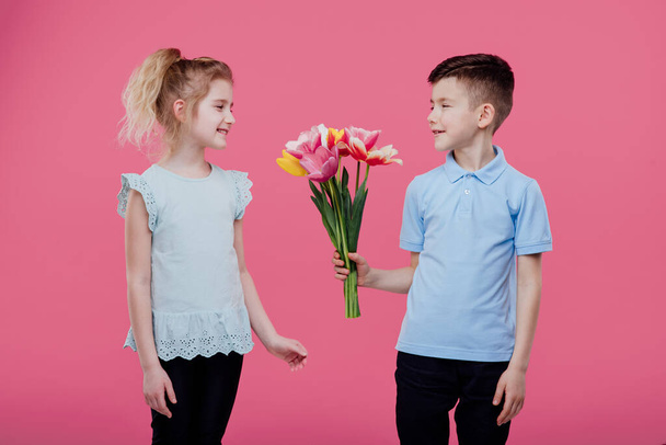 boy stretches flowers to a little girl in pink dress - Zdjęcie, obraz