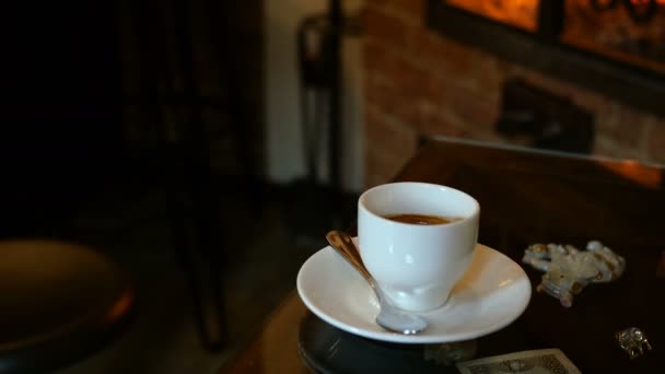 Eine Tasse Kaffee steht im Café oder Restaurant mit Kamin auf dem Tisch. Flammenschimmer spiegeln sich auf dem Tisch. Romantischer Rahmen. Selektiver Fokus. Mittelfristiger Plan. - Filmmaterial, Video