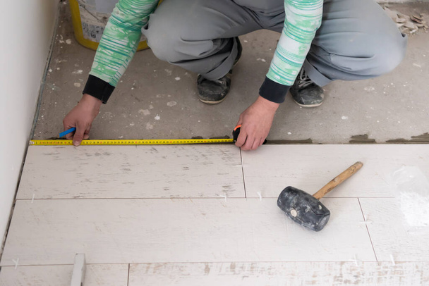 Facharbeiter bei der Verlegung der Keramik-Holz-Effekt-Fliesen auf dem Fußboden Arbeiter bei der Herstellung von Laminatböden auf der Baustelle der neuen Wohnung - Foto, Bild