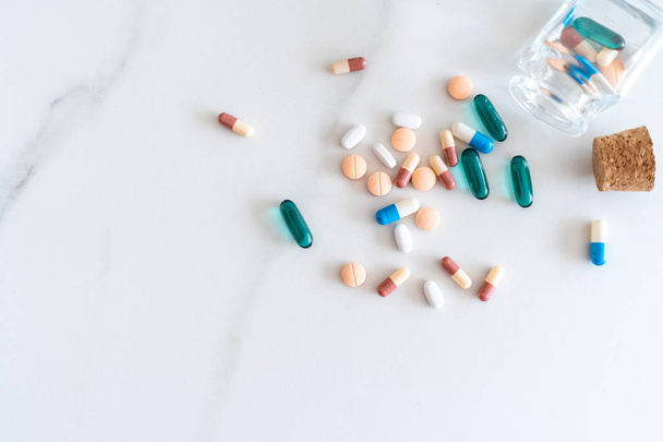 Bovenaanzicht van medicijnen tabletten giet uit pillen fles van marmer textuur witte achtergrond. Gezondheidszorg medische levensstijl trendconcept. - Foto, afbeelding