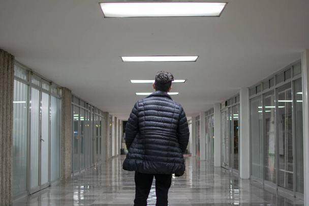 Homem de pé dentro de um túnel com luzes brancas vestindo uma jaqueta azul e jeans pretos
 - Foto, Imagem