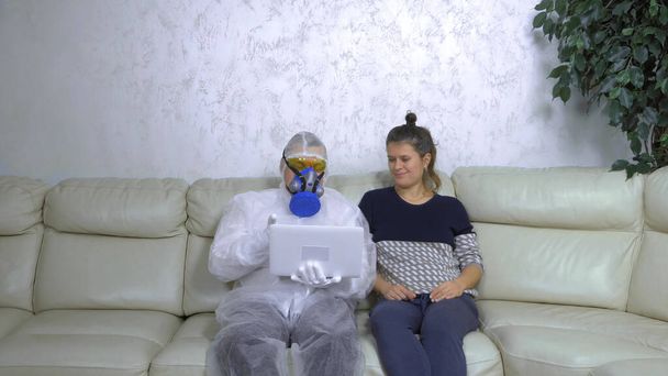 a man in a protective suit uses a laptop next to a woman in casual clothes - Фото, изображение