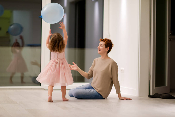 happy family spending time together young redhead mother and cute little daughter having fun while playing with balloons near the window on beautiful evening at home - Fotoğraf, Görsel