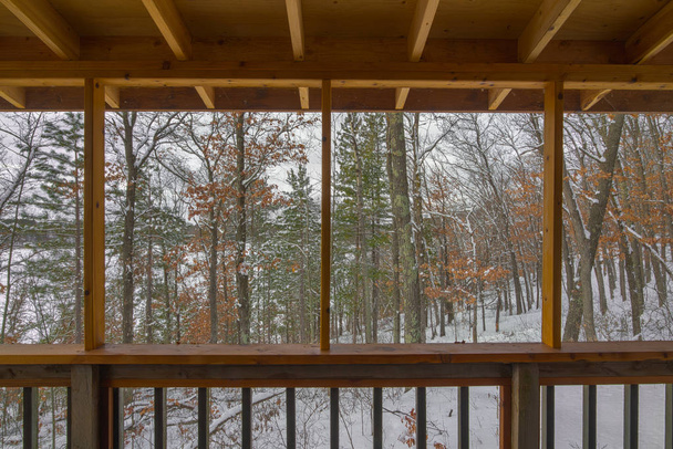Hermosa vista nevada de invierno de un bosque mixto de Northwoods (caducifolios y coníferas) a través de un porche protegido en una cabaña rústica frente a un lago remoto en el norte de Wisconsin
 - Foto, imagen