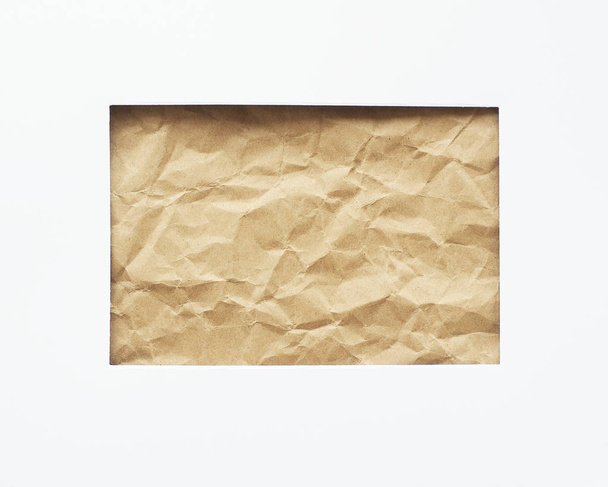Een rechthoekig gat in een wit vel papier. Verfrommeld ambachtelijk papier op de achtergrond. Ruimte voor kopie - Foto, afbeelding