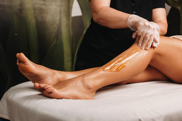 Caucasian spa professional having a sugaring session on legs for a charming woman - Photo, Image