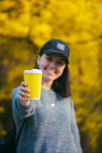 νεαρή όμορφη γυναίκα κρατώντας και δείχνοντας κίτρινο φλιτζάνι καφέ χαρτί. αντίγραφο χώρου. ελεύθερος χώρος - Φωτογραφία, εικόνα