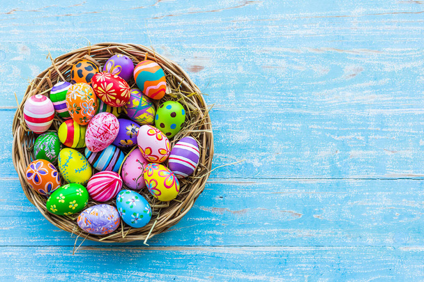 Concepto de vacaciones de Pascua, huevos de Pascua coloridos en cesta sobre fondo de madera rústica de color pastel azul con espacio
. - Foto, imagen