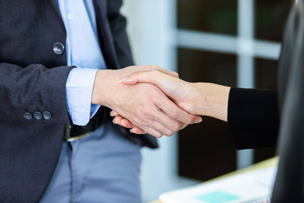 Деловая женщина и бизнесмен пожимают друг другу руки в офисе на заднем плане после подписания контракта или рукопожатия сделки, бизнес выразил уверенность смелые и успешные концепции - Фото, изображение