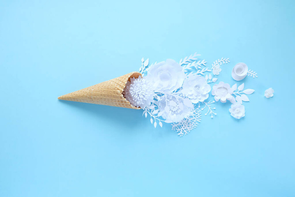 Hand holds a waffle cone with white paper flowers on light blue background. Holiday concept. - Фото, изображение