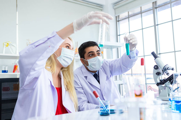 Δύο επιστήμονες εργάζονται κρατώντας κοιτάζοντας δοκιμαστικό σωλήνα με δείγμα σε έναν επιστήμονα εργαστηρίου χημείας ή νεαρή γυναίκα και άνδρας ερευνητής κάνουν έρευνες στο υπόβαθρο εργαστηριακής ανάλυσης - Φωτογραφία, εικόνα