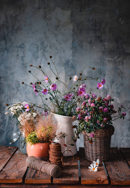 Beautiful bouquets of wildflowers on a wooden table on a cold concrete wall background. Simple floral arrangements made by a florist in a rustic style. free space - Фото, зображення