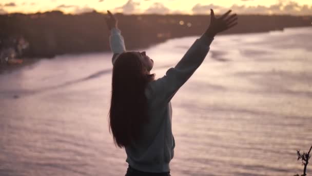 close-up portret van mooie jonge vrouw kijken omhoog raise armen met wind waait haar genieten van rustige zee bij zonsondergang 4k - Video