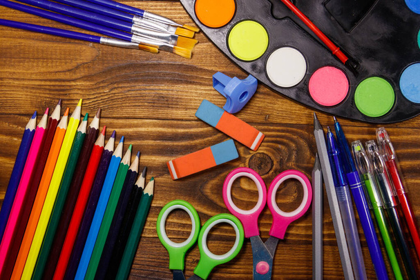 Set of school stationery supplies. Colored pencils, watercolor paints, paintbrushes, pens, scissors, eraser, sharpener on wooden desk. Back to school concept - 写真・画像