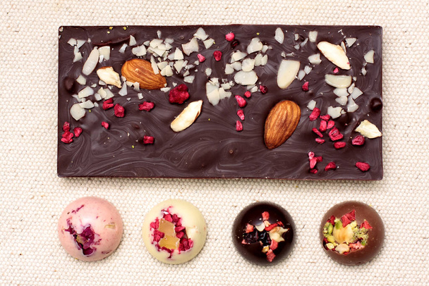 Ručně vyráběné bílé, mléčné a tmavé čokoládové tyčinky a bonbóny s různými sušenými ovocnými a ořechovými polevy na textilním pozadí - Fotografie, Obrázek