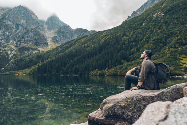 człowiek siedzi na skale przed jeziorem w górach ciesząc się koncepcją wędrówki widokowej - Zdjęcie, obraz