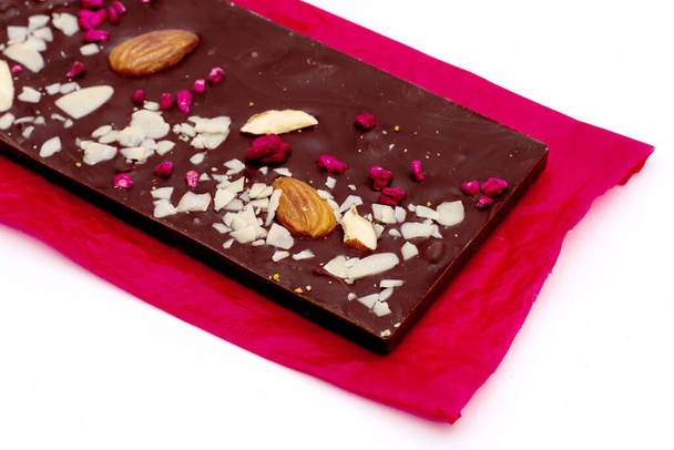 Ручная белая, молочная и темно-шоколадная плитка с различными фруктовыми и ореховыми начинками на красной бумаге на белом фоне
 - Фото, изображение