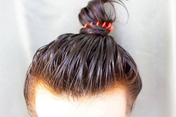 Hair care at home. The girl applied the balm to her hair and gathered her hair into a bun. - Photo, Image