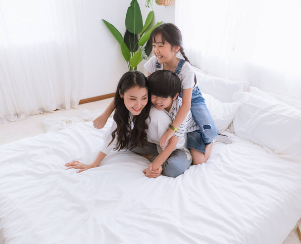 Krásná šťastná asijská rodina v útulném domově. Usmívající se matka, syn a dcera si užívají, odpočívají a hrají si spolu v ložnici. Šťastný vztah a sblížení lásky mezi rodiči a dětmi moment - Fotografie, Obrázek