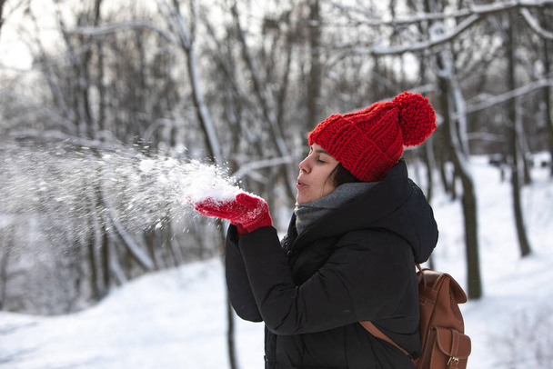 joven bastante sonriente mujer en abrigo de invierno con sombrero rojo en el parque forestal de la ciudad tiempo nevado
 - Foto, Imagen