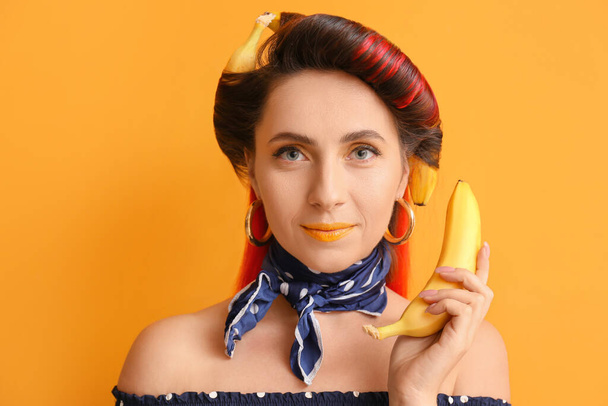 Όμορφη γυναίκα με μπανάνες στα μαλλιά της στο φόντο χρώμα - Φωτογραφία, εικόνα