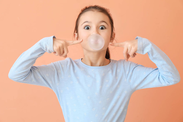 Cute little girl with chewing gum on color background - Photo, Image