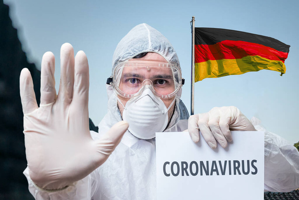 Medico in tuta avverte di infezione coronavirus in Germania. Bandiera tedesca sullo sfondo
. - Foto, immagini