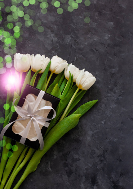 Witte tulp bloemen en zwarte geschenkdoos op donkere achtergrond plat gelegd. Plaats voor tekst 8 maart Happy Womens Mothers Day.Bloemenboeket met zilveren lint, wenskaart.Kopieer ruimte website banner top view - Foto, afbeelding