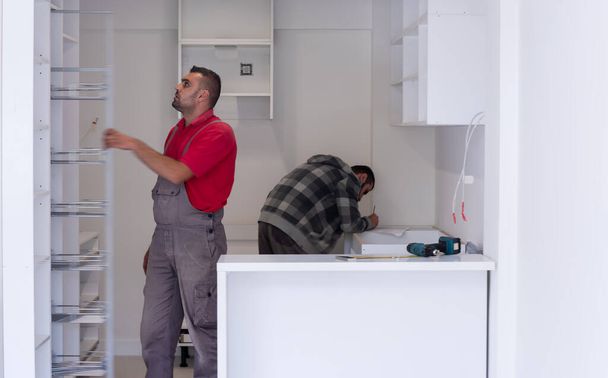 two professional workers installing a new stylish modern kitchen furniture - Zdjęcie, obraz
