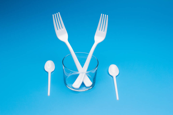 Cutlery for eating white and made of plastic and transparent glass cups; Cutlery and glasses teaspoons for coffee and for rationing small amounts of sugar, fork for pricking food, glasses for drinking - Fotografie, Obrázek