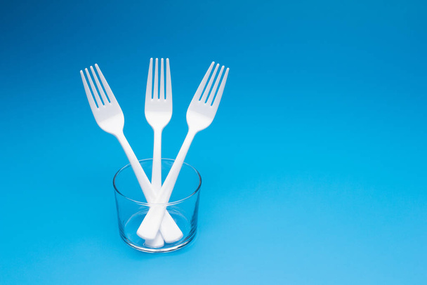Cutlery for eating white and made of plastic and transparent glass cups; Cutlery and glasses teaspoons for coffee and for rationing small amounts of sugar, fork for pricking food, glasses for drinking - Foto, afbeelding