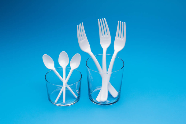 Cutlery for eating white and made of plastic and transparent glass cups; Cutlery and glasses teaspoons for coffee and for rationing small amounts of sugar, fork for pricking food, glasses for drinking - Fotó, kép