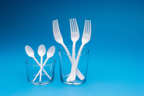 Cutlery for eating white and made of plastic and transparent glass cups; Cutlery and glasses teaspoons for coffee and for rationing small amounts of sugar, fork for pricking food, glasses for drinking - Fotó, kép