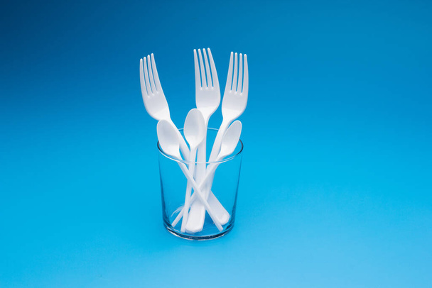 Cutlery for eating white and made of plastic and transparent glass cups; Cutlery and glasses teaspoons for coffee and for rationing small amounts of sugar, fork for pricking food, glasses for drinking - Zdjęcie, obraz