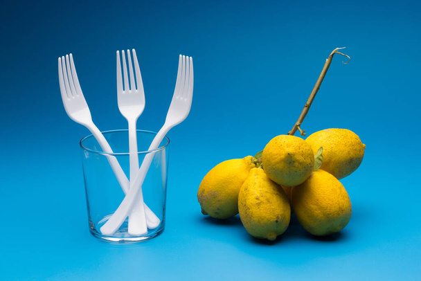 Healthy lemons with an acid flavor and full of vitamins, together with plastic cutlery; Citrus lemons on blue background. - Photo, Image